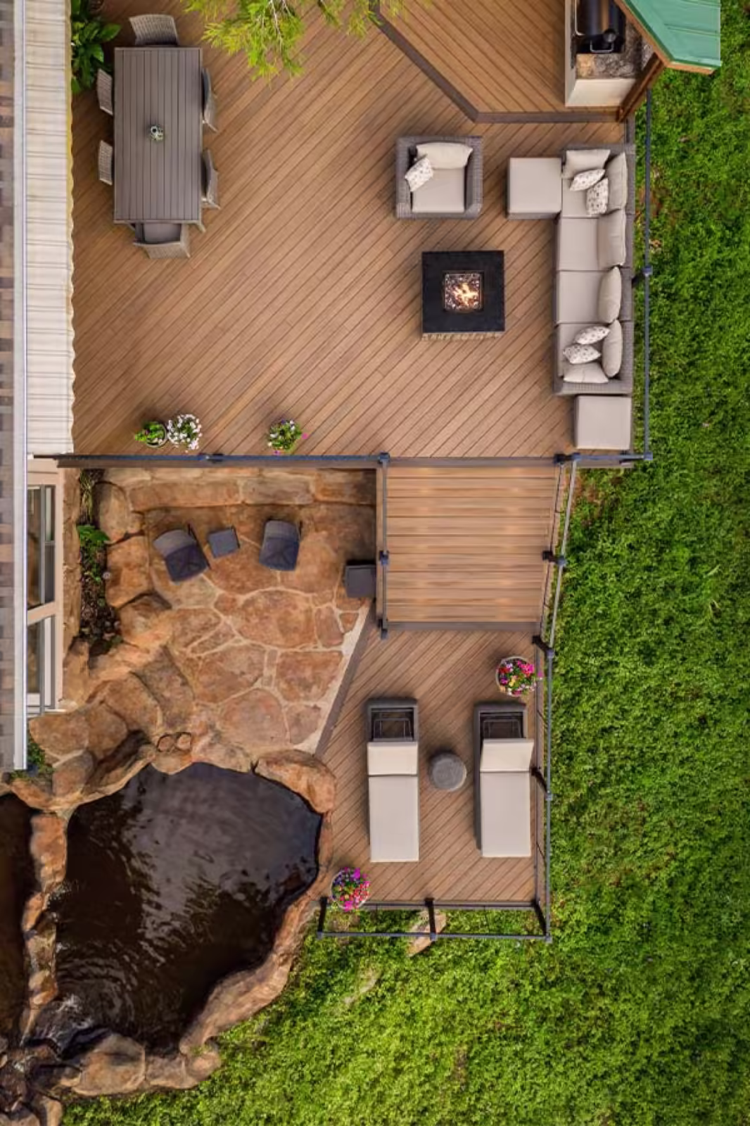 Aerial view of a multi-level composite deck with dining area, fire table, lounge seating and a flagstone waterfall pond