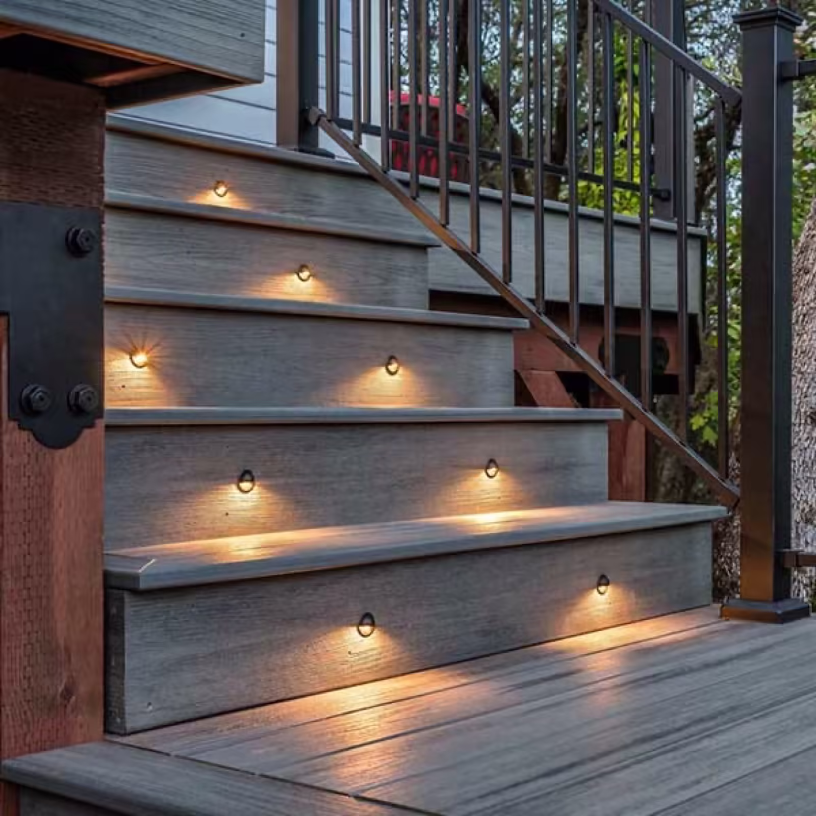 Weathered gray composite deck stairs lit by recessed step lights at dusk, framed by a black aluminum railing